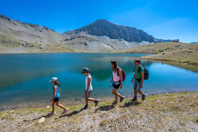 Famille en randonnée au bord d'un lac turquoise du Monde des 6 Lacs à Orcières Merlette
