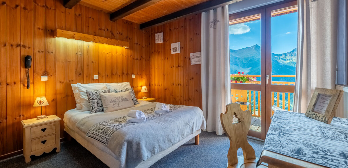 Lit double avec tête de lit en bois et porte-fenêtre ouvrant sur un balcon avec vue sur les montagnes