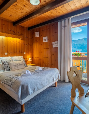 Lit double avec tête de lit en bois et porte-fenêtre ouvrant sur un balcon avec vue sur les montagnes