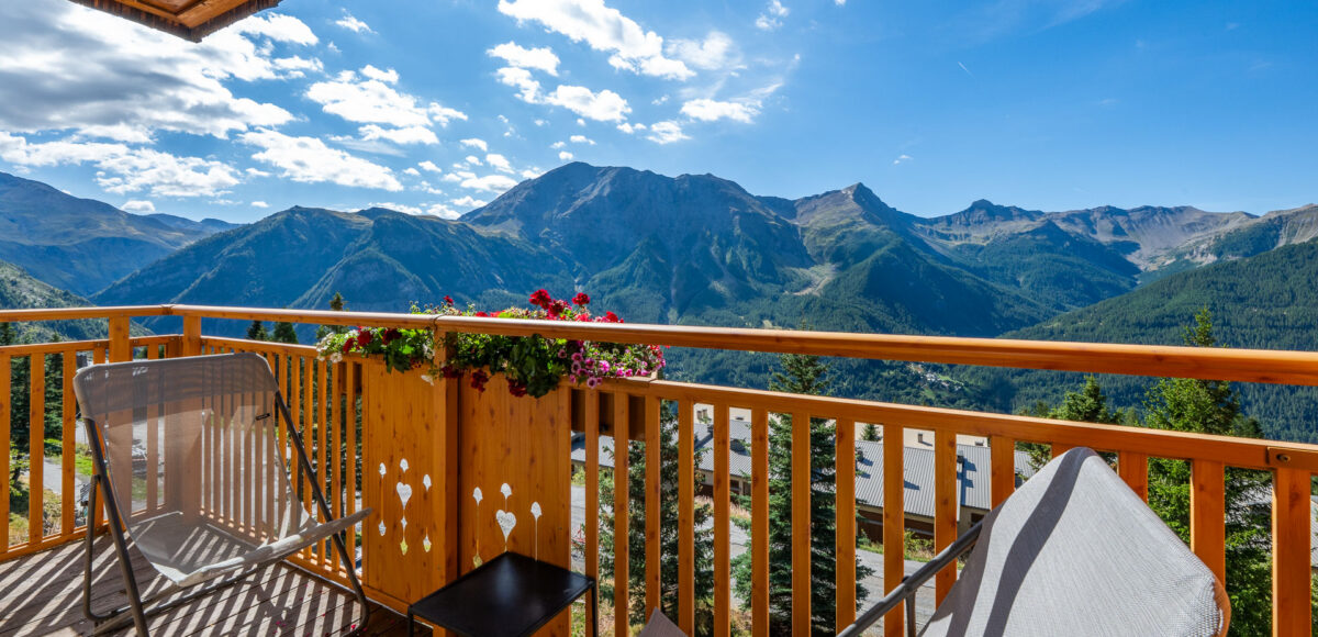 Balcon en bois avec chaises longues, jardinière fleurie et vue panoramique sur les sommets