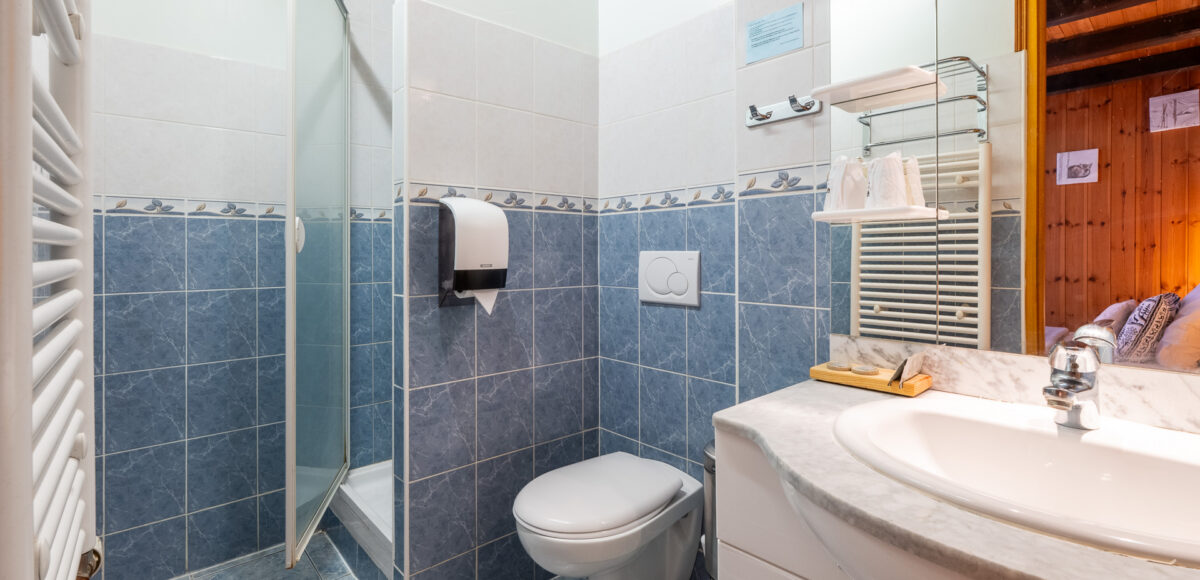 Salle de bain carrelée en bleu avec douche vitrée, WC suspendu et vasque sur meuble blanc