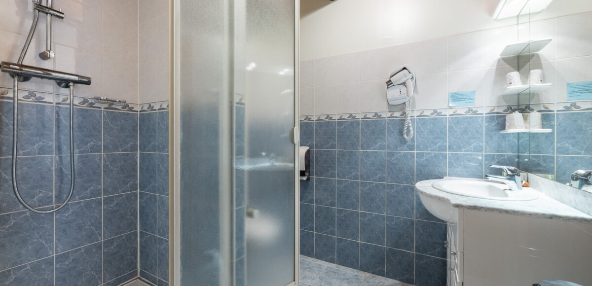 Salle de bain avec douche à l'italienne vitrée, vasque et sèche-cheveux mural sur fond carrelé bleu