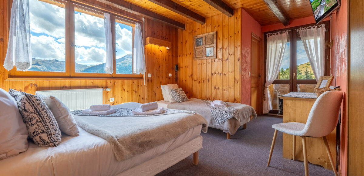 Chambre Triple Confort avec deux lits, mur orangé et télévision murale face à la fenêtre
