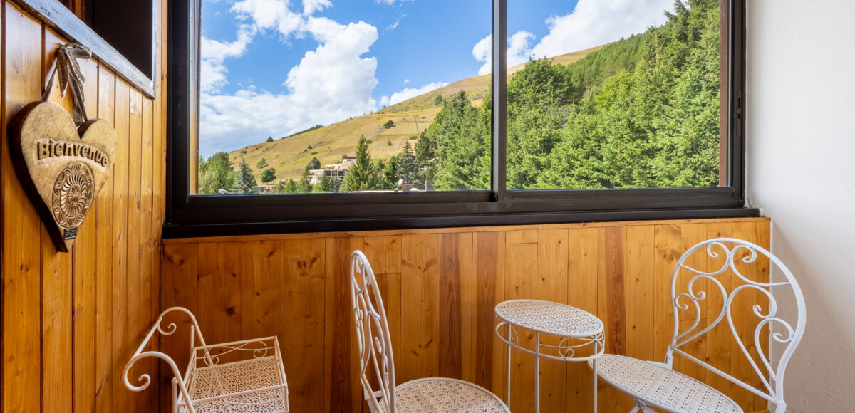 Balcon meublé de chaises en fer forgé blanc avec vue sur la forêt et les montagnes