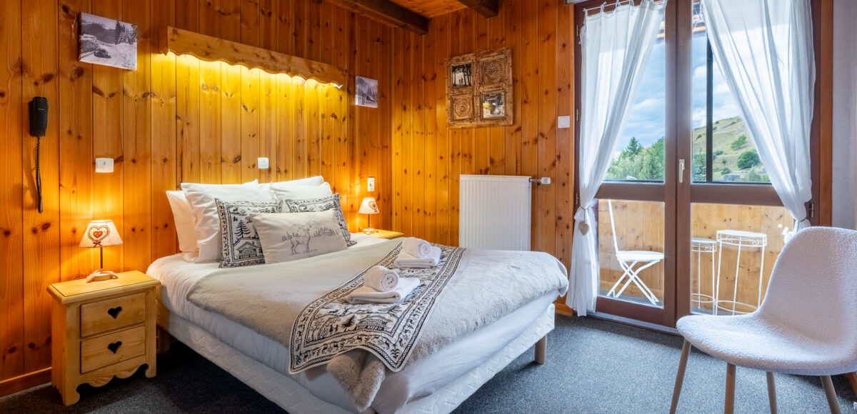 Lit double avec tête de lit en bois sculpté et porte-fenêtre donnant sur un balcon montagne