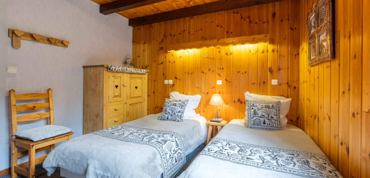 Lits jumeaux aux coussins motifs de cerfs devant une armoire en bois à cœurs sculptés