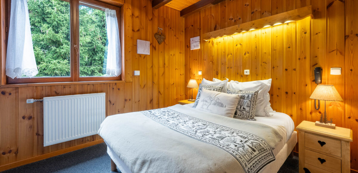 Lit double aux coussins motifs de cerfs face à une fenêtre donnant sur les sapins