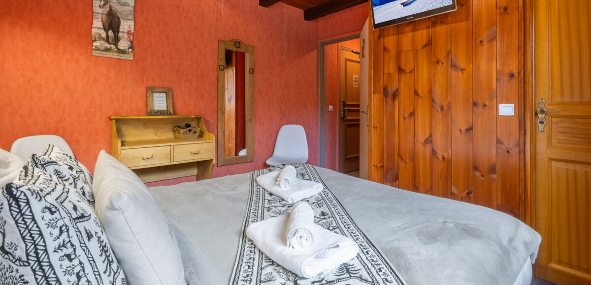 Lit double aux draps gris avec téléviseur mural et mur orange