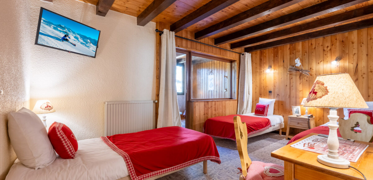 Chambre avec lits simples à couvertures rouges, télévision murale et coin bureau en bois