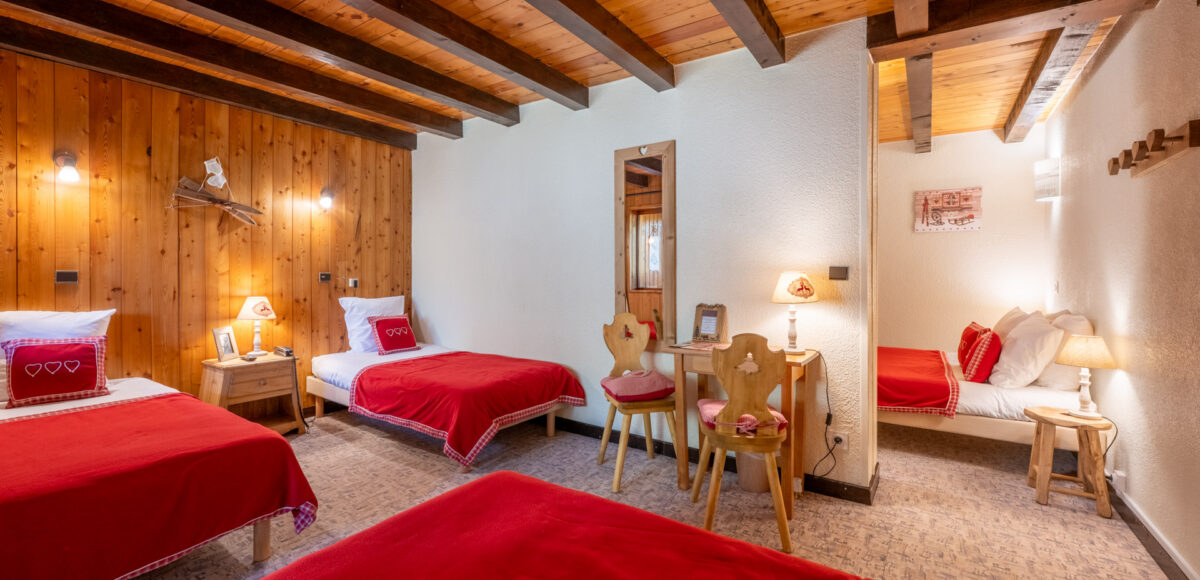 Chambre familiale avec trois lits simples à couvertures rouges sous plafond à poutres en bois