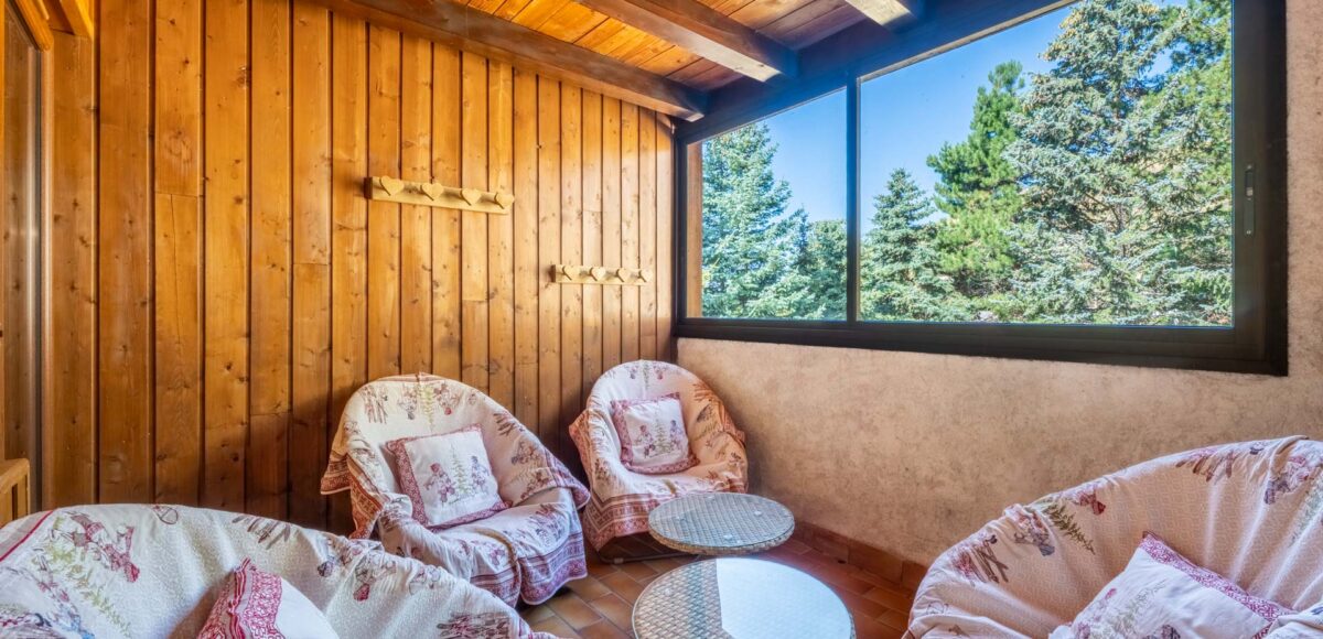 Coin salon mansardé avec fauteuils à motifs montagnards et vue sur les sapins par la fenêtre