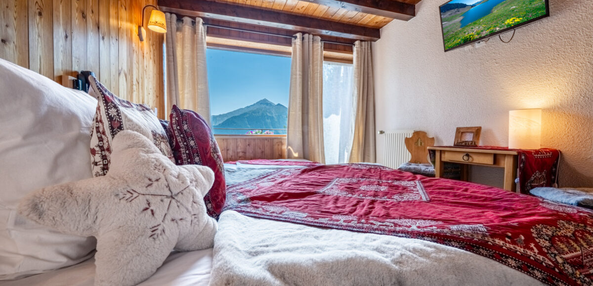 Lit avec coussin étoile en fourrure et plaid rouge, vue sur les montagnes