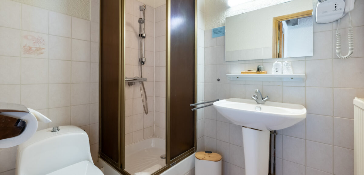 Salle de bain avec cabine de douche dorée, lavabo sur pied et sèche-cheveux