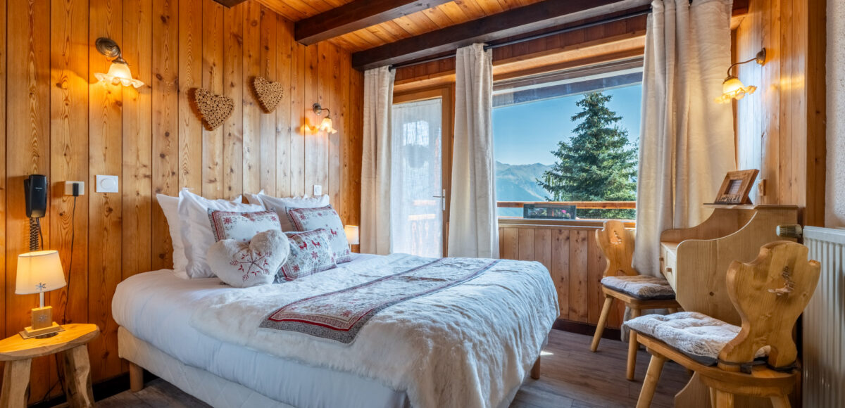 Lit double avec coussins brodés de cerfs et vue sur sapins et montagnes par la fenêtre