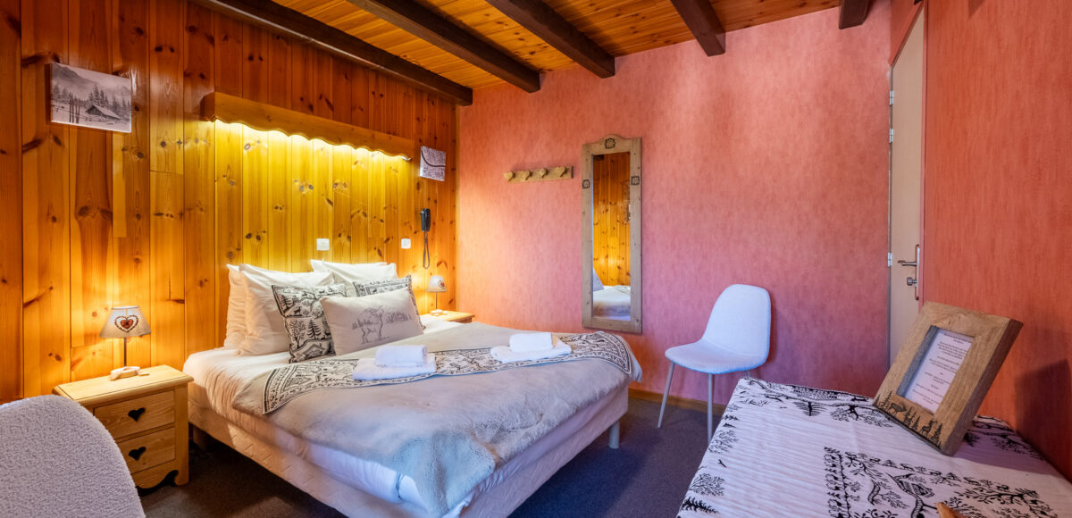 Lit double dans une chambre aux murs roses avec miroir en bois et chaise blanche